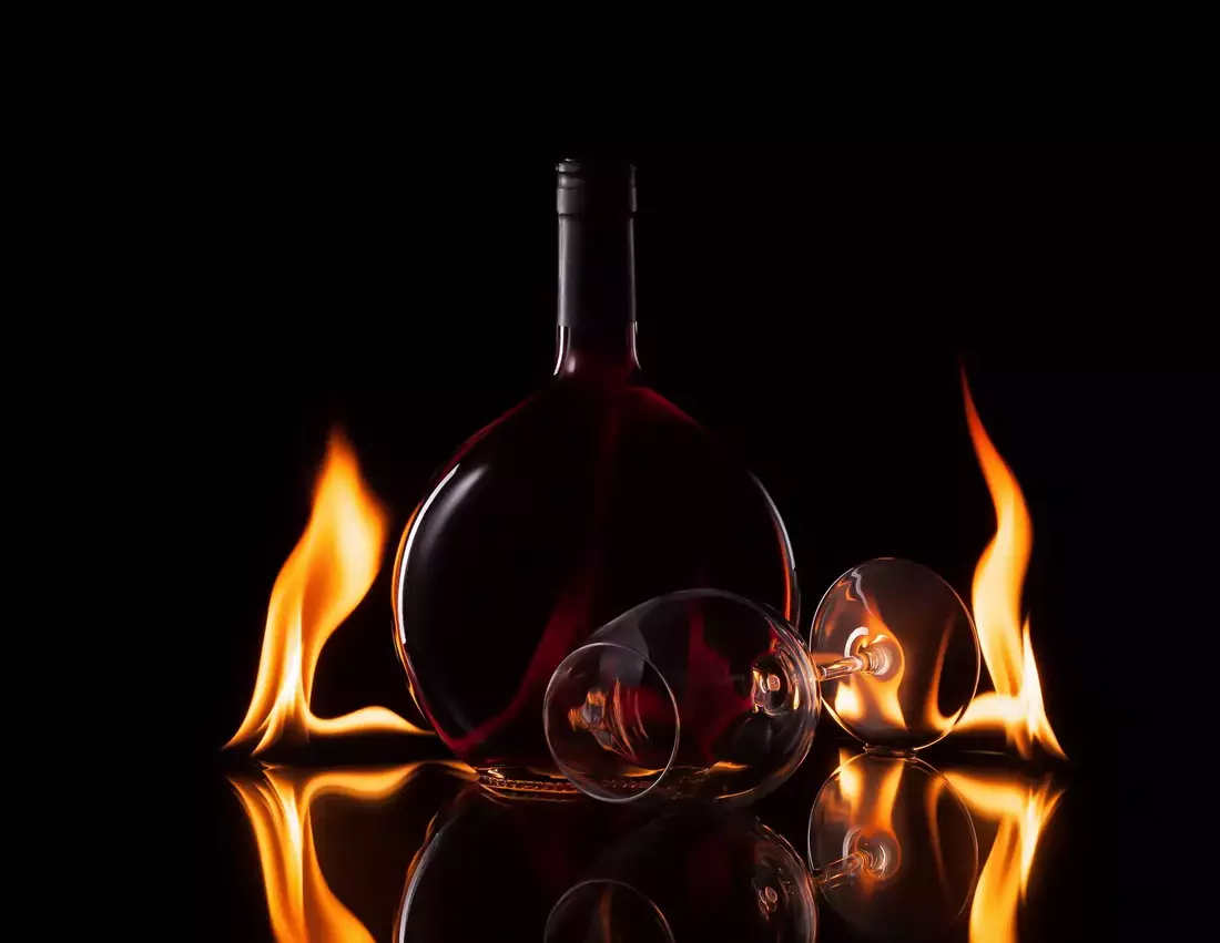 Bottle and glass of wine in fire flame on black background Bottle and glass of wine in fire flame on black background